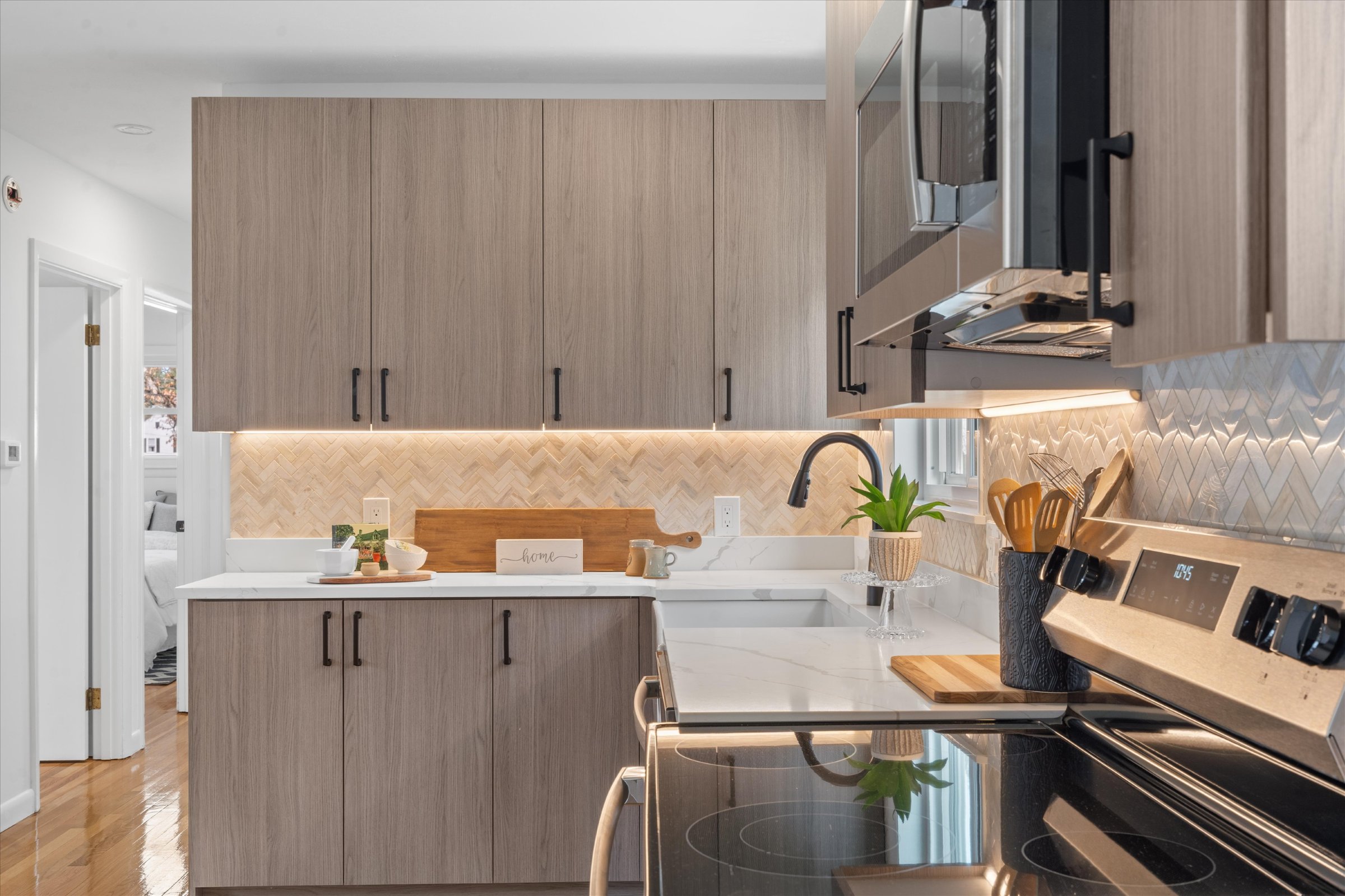 Wood-grain slab kitchen cabinets with black pulls, herringbone tile backsplash, and white quartz countertops