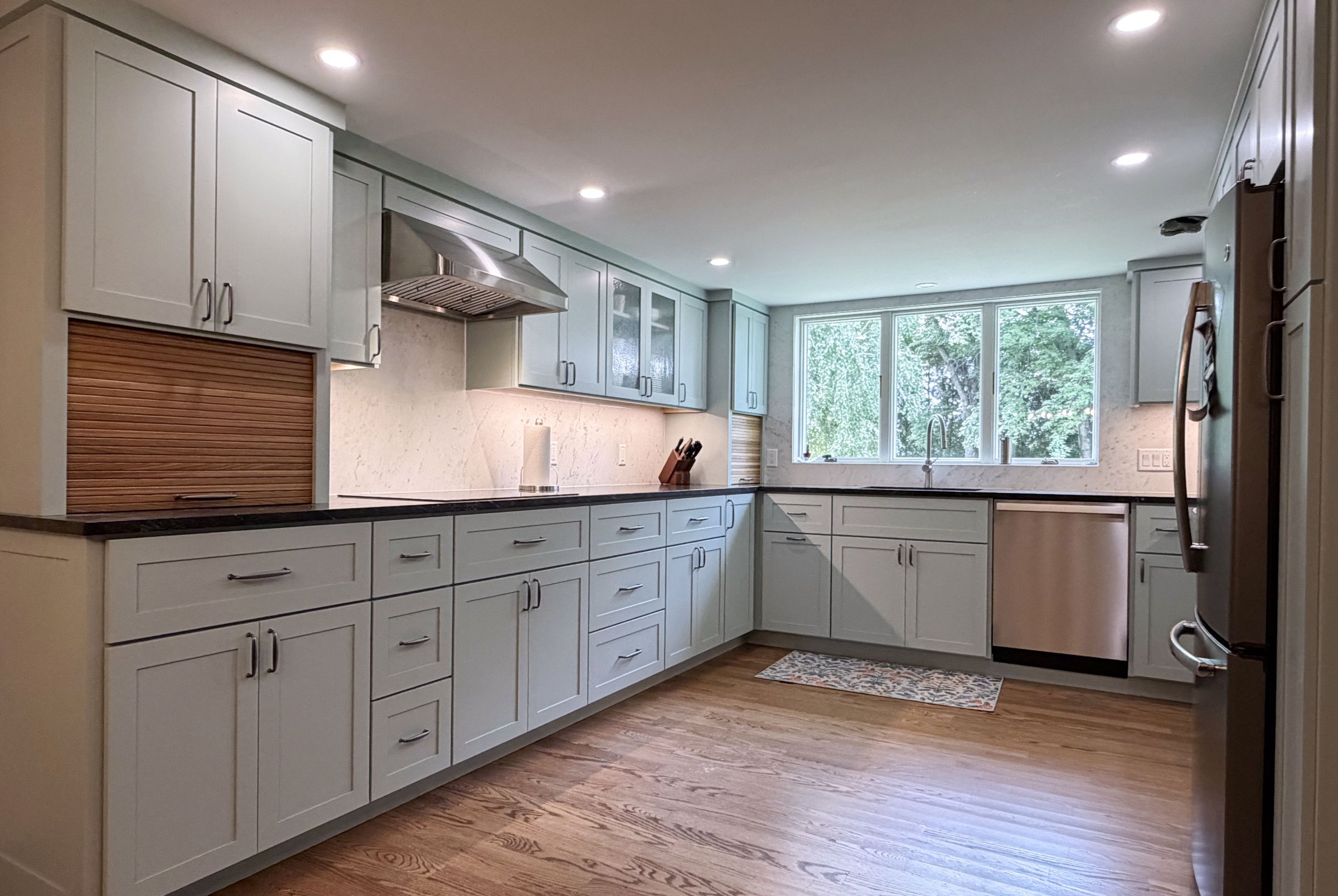 Sage green shaker kitchen with a wood tambour appliance garage, stainless range hood, and dark countertops